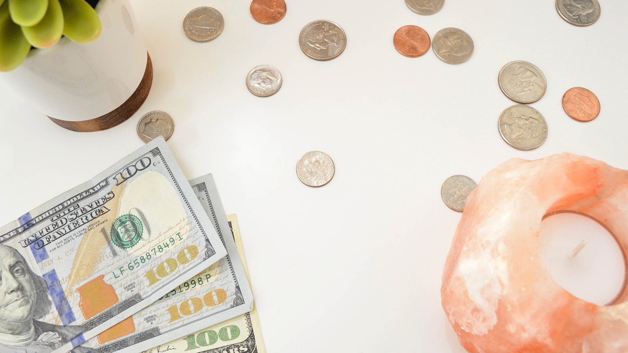 Cash and Coins Scattered on Desk with Plant and Candle