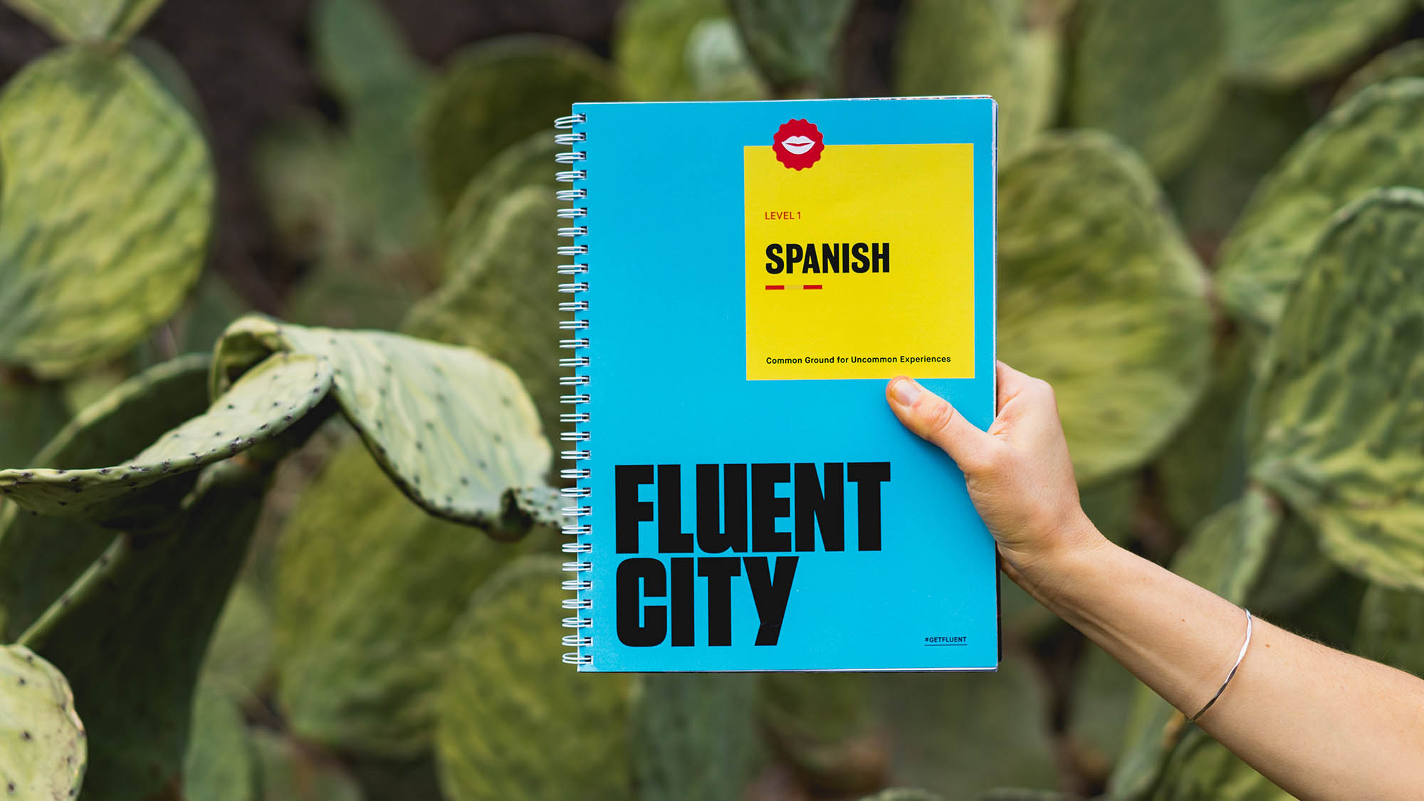 Arm Holding Blue Fluent City Spanish Language Book with Cactus Background