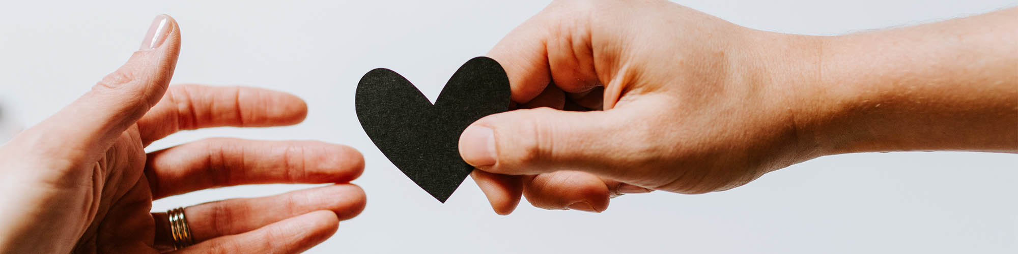 One Hand Giving Black Paper Heart to Second Hand
