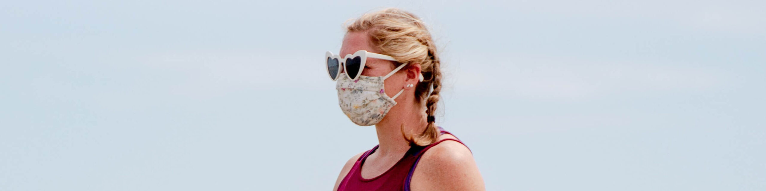 Headshot of blonde woman with surgical mask and sunglasses on beach