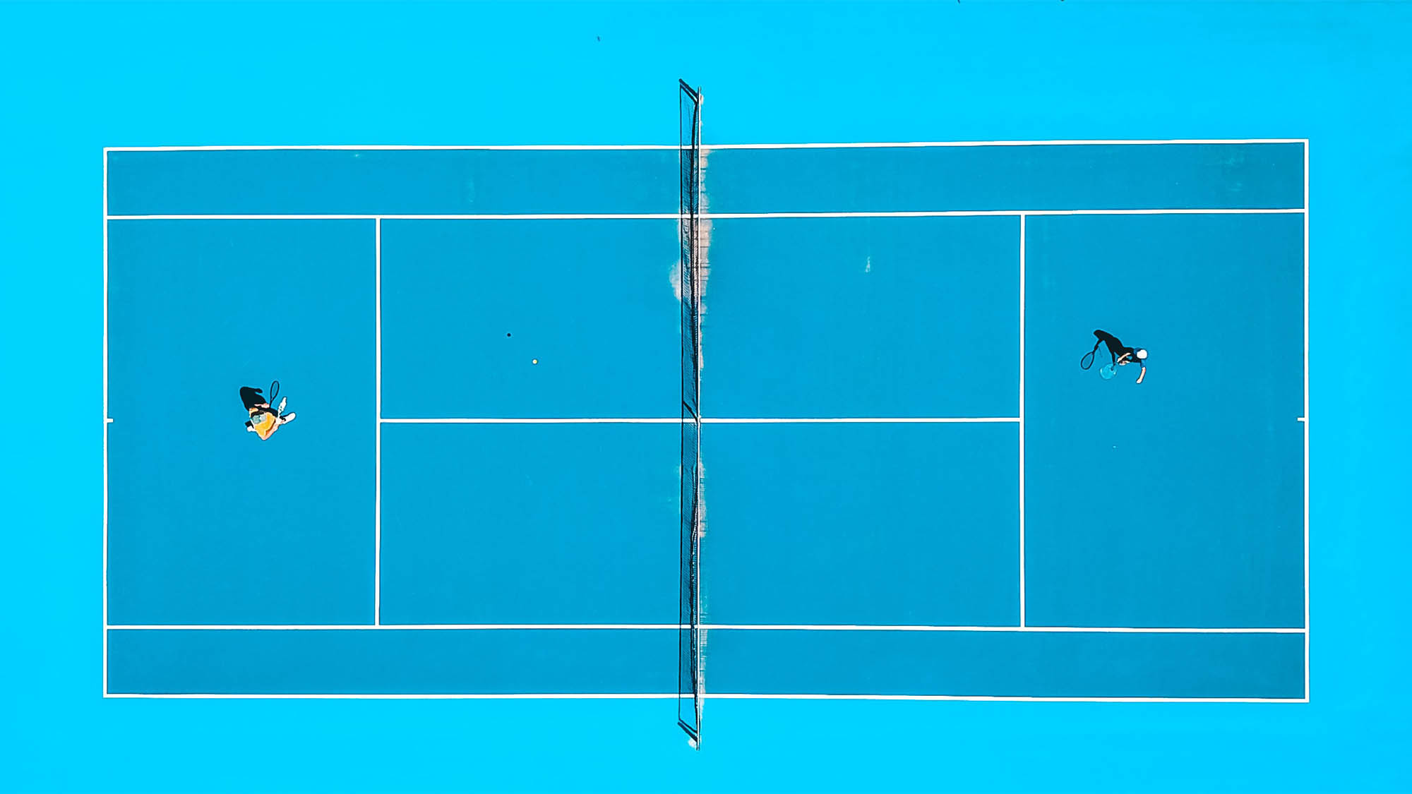 Aerial shot of two people playing tennis on teal court