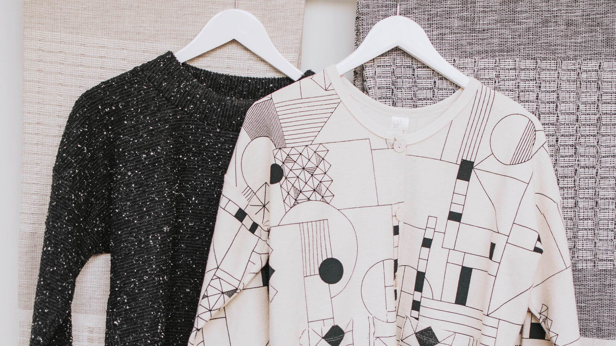 Black knit sweater hanging beside white sweater with geometric print