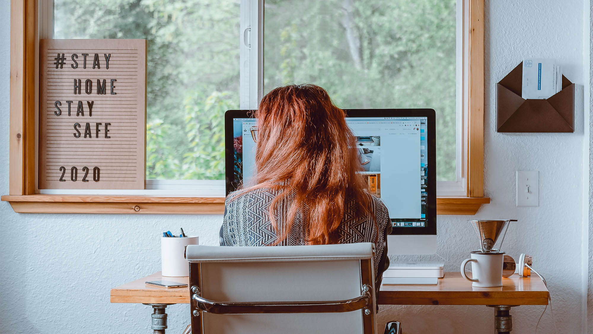 Back of Long Redheaded Woman Seated at Home Office Desk with Window in Background