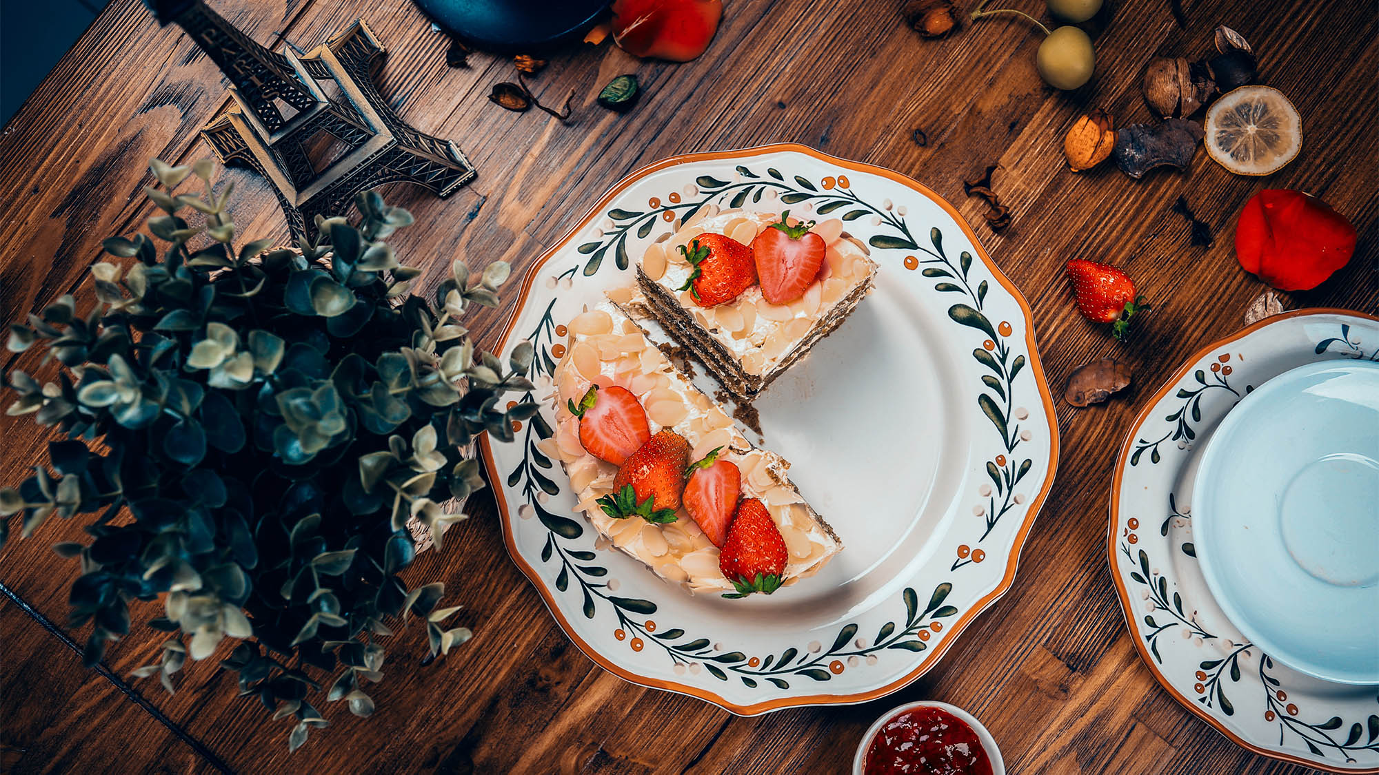 Fruit cake topped with strawberries and one slice missing next to plant and other table decorations