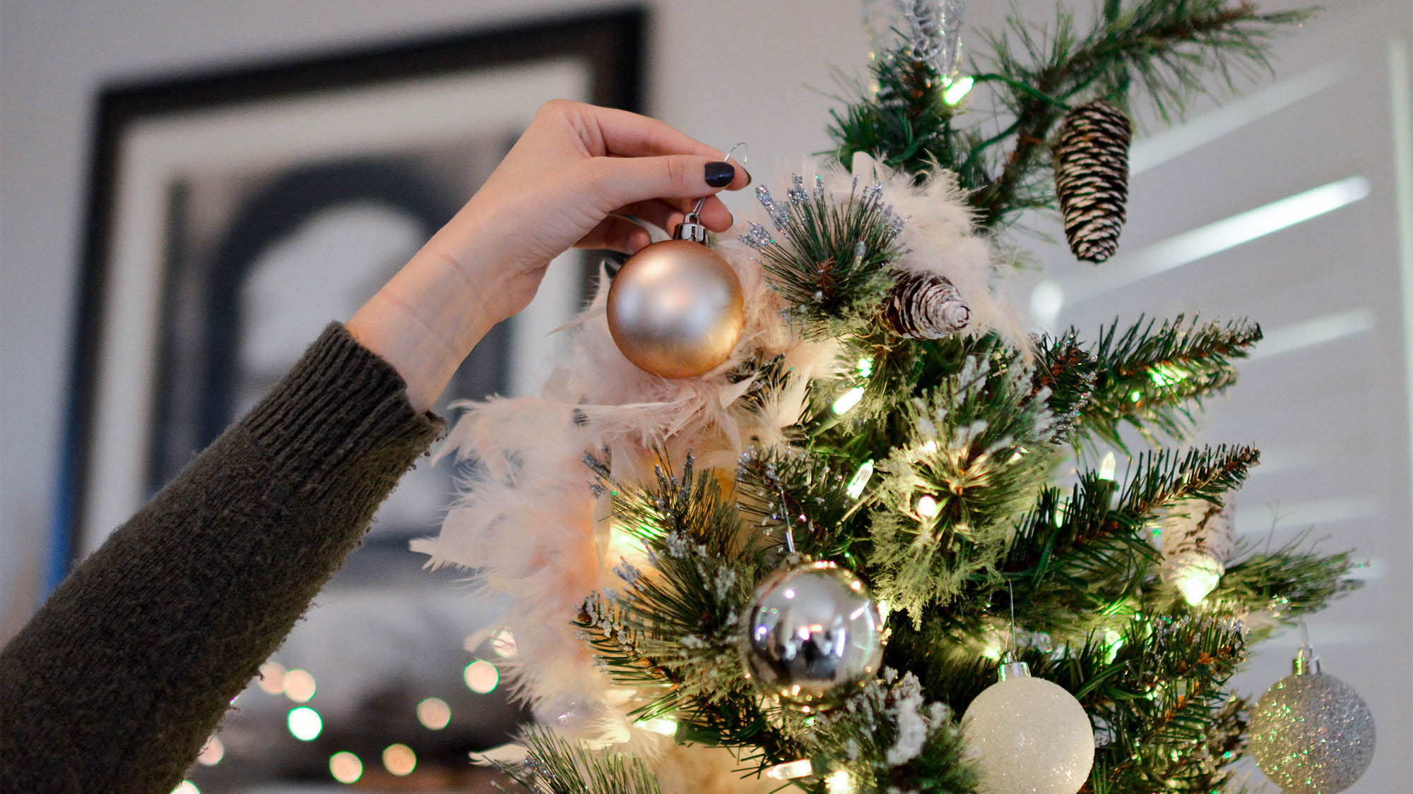 White woman's hand putting glass ornament on decorated Christmas tree