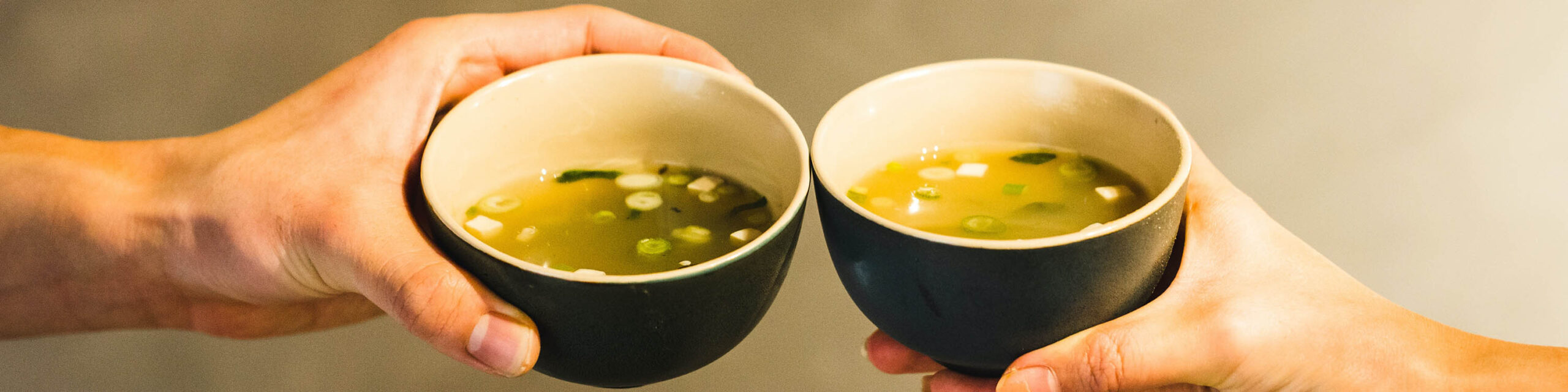 Two white hands cheersing with two cups of miso soup