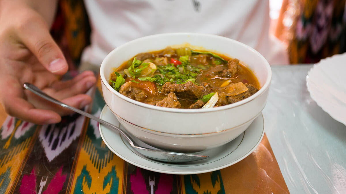 Lagman soup bowl with white hand touching spoon