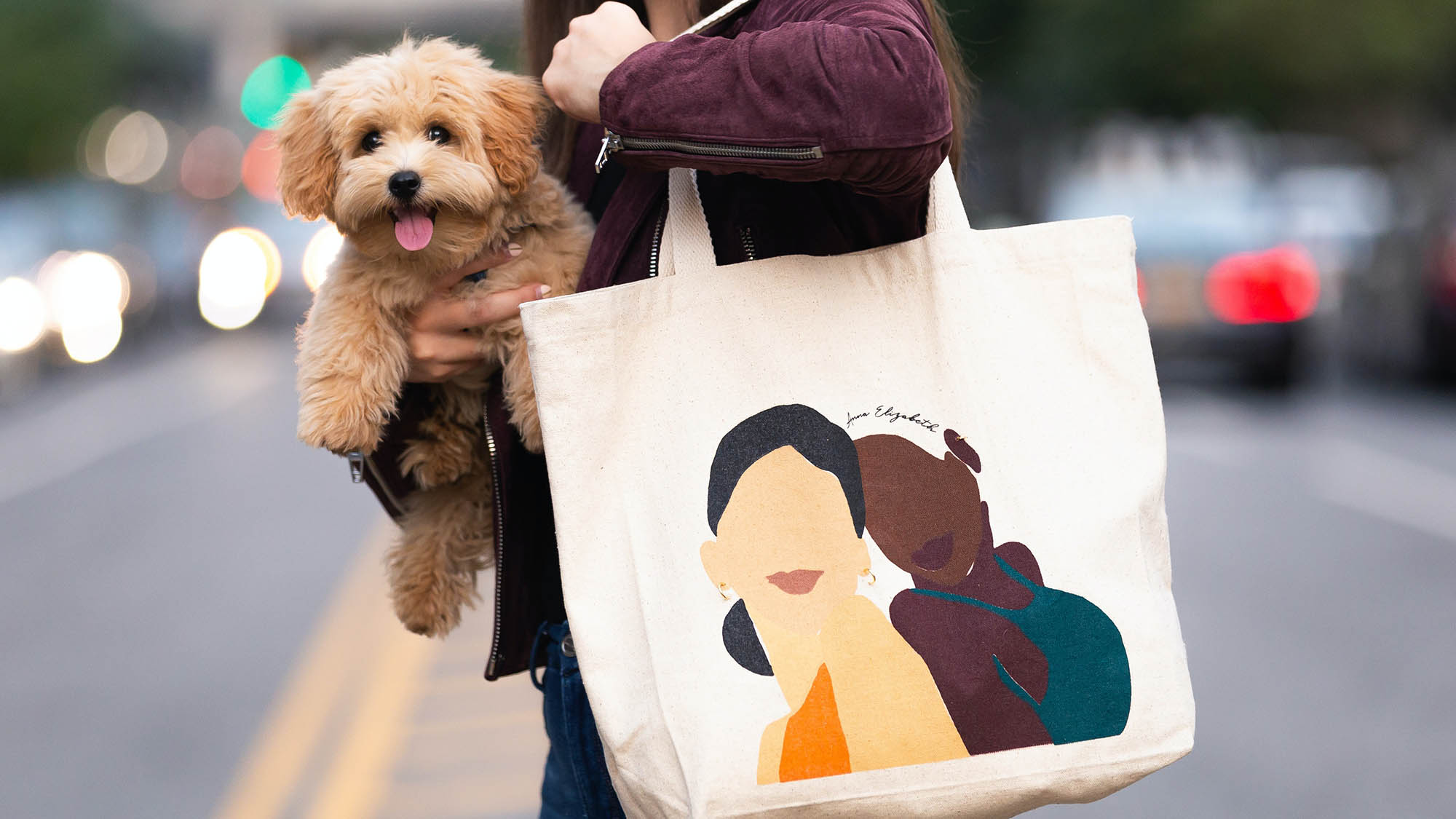 Woman on NYC street holding brown puppy and tote bag with two illustrated women 