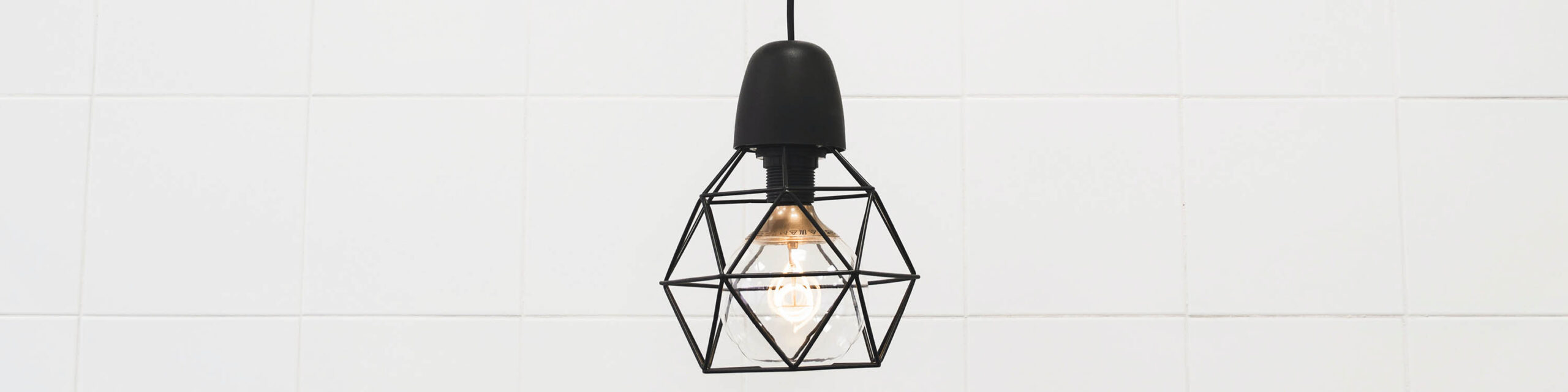 Black geometric light fixture against white tile backsplash