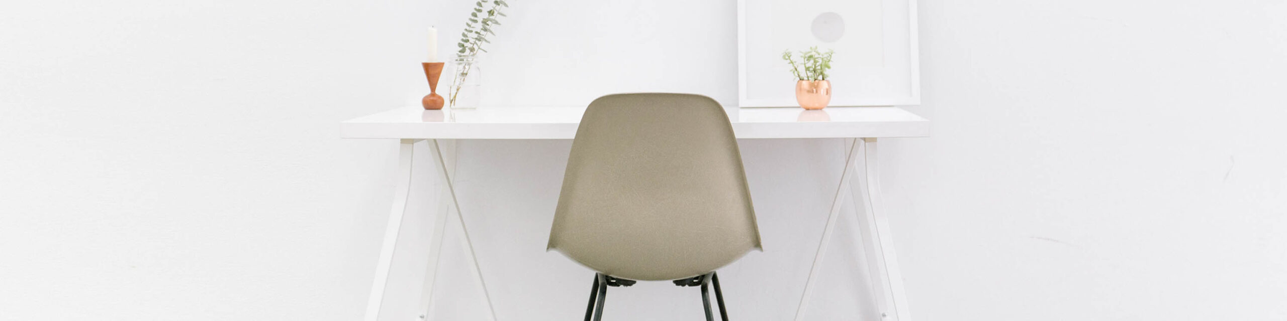 White minimalist desk with eucalyptus and succulent, gray chair, and white wall and white wall art in background