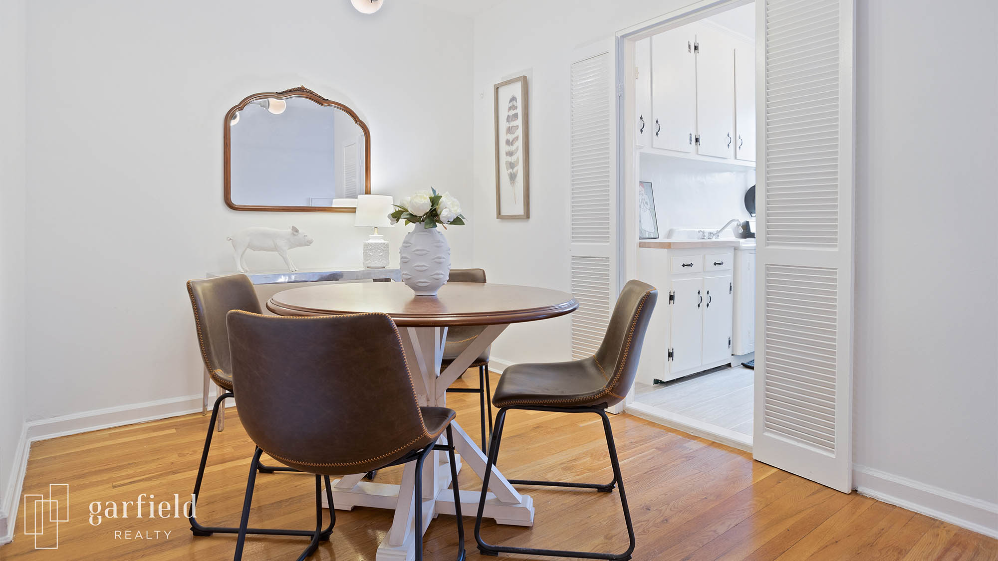 Staged dining room with four brown chairs and vase on table, wall mirror in background