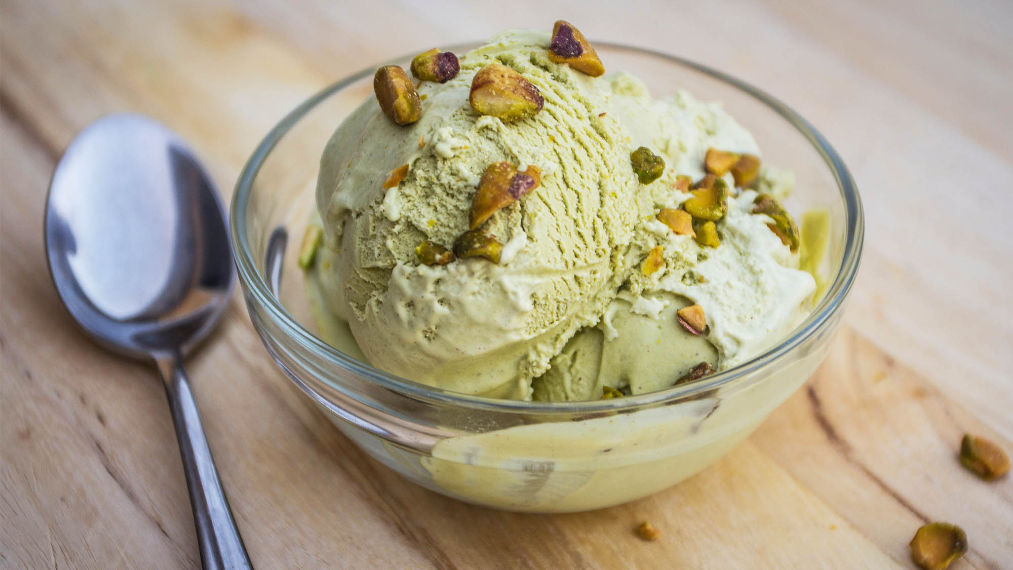 Clear glass dish of pistachio ice cream with spoon resting beside it on wood table
