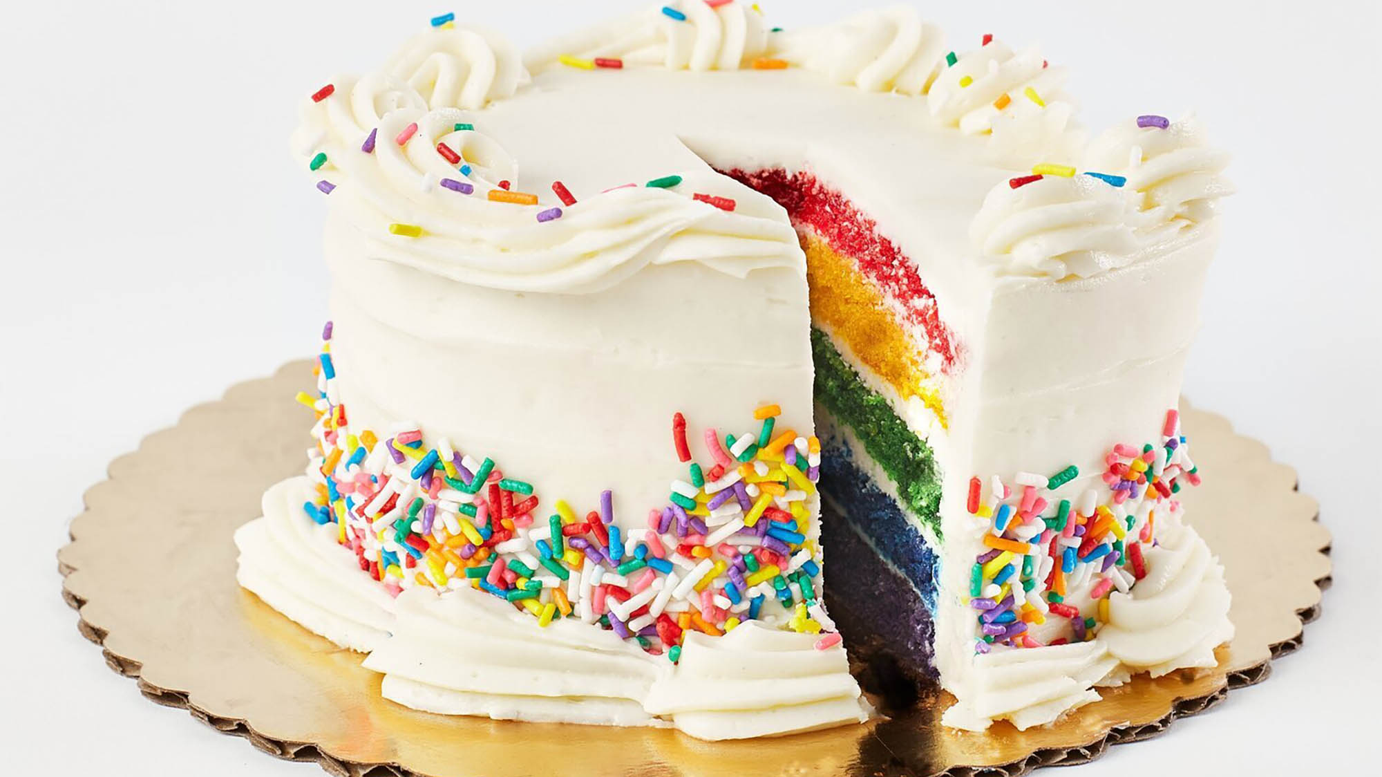 White cake with rainbow sprinkles with one missing piece revealing rainbow layers inside