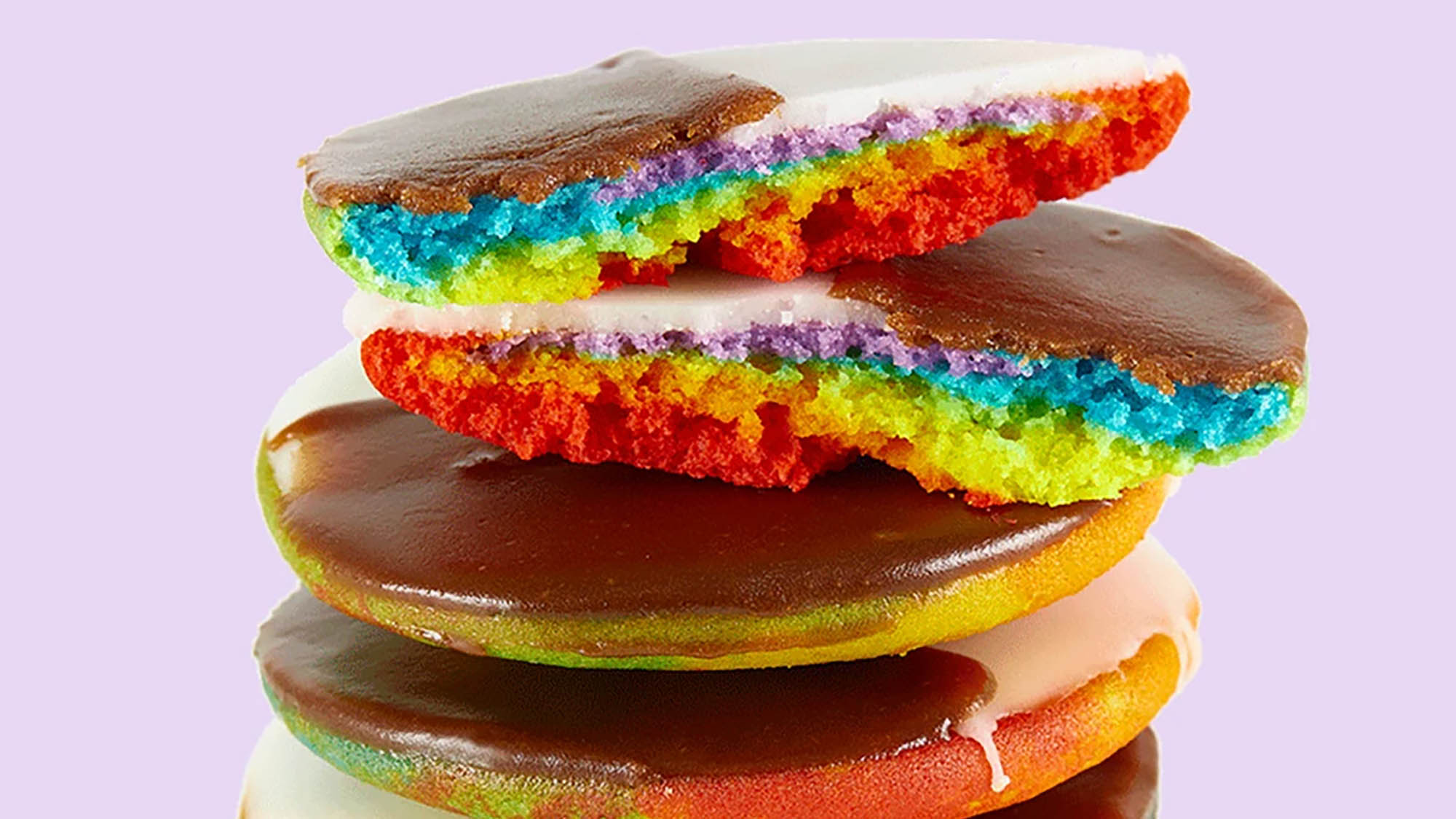 Stack of rainbow cookies with brown and white icing and top cookie broken in two pieces