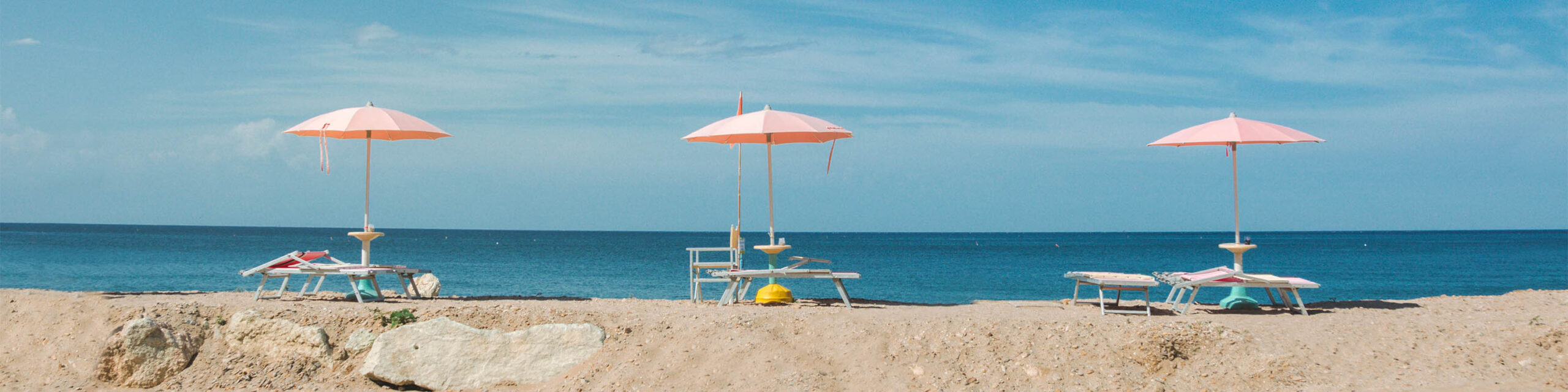 Three pink beach umbrellas on sand overloooking the ocean