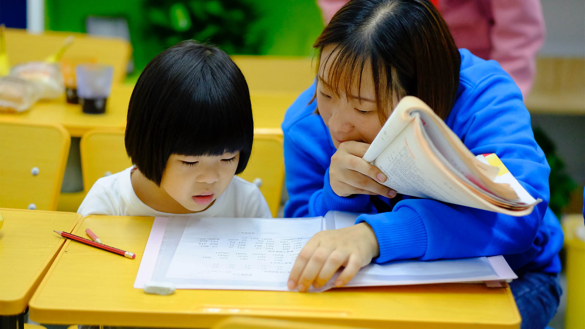 Asian woman tutoring Asian girl at desk