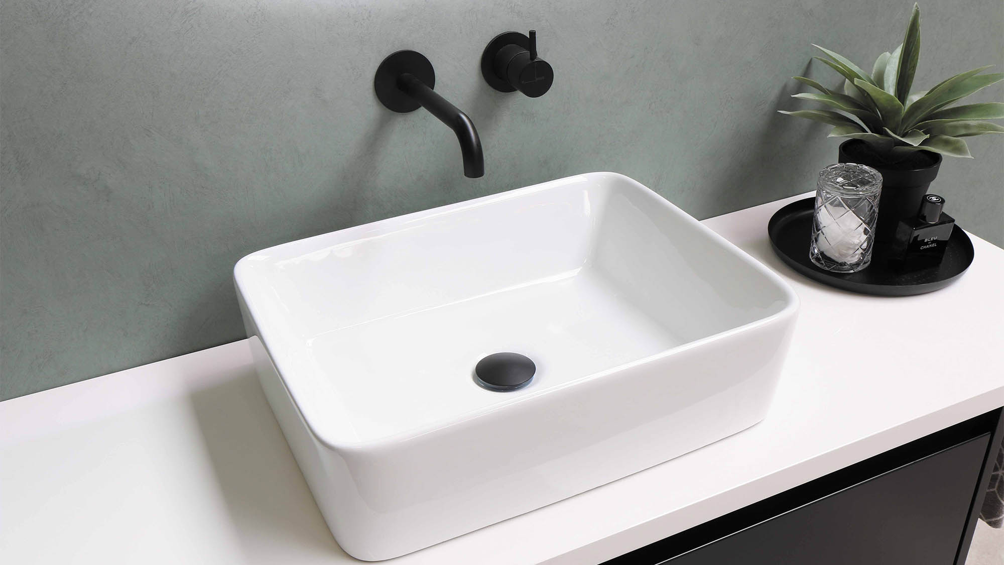 White bathroom sink with modern black wall faucet and succulent planter to the right