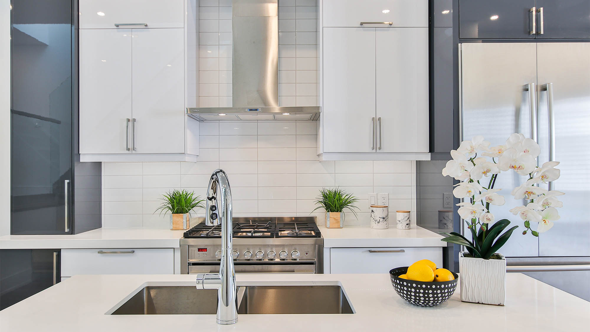 Stainless steel oven and hood flanked by white cabinets with white tile backsplash and view from over kitchen sink