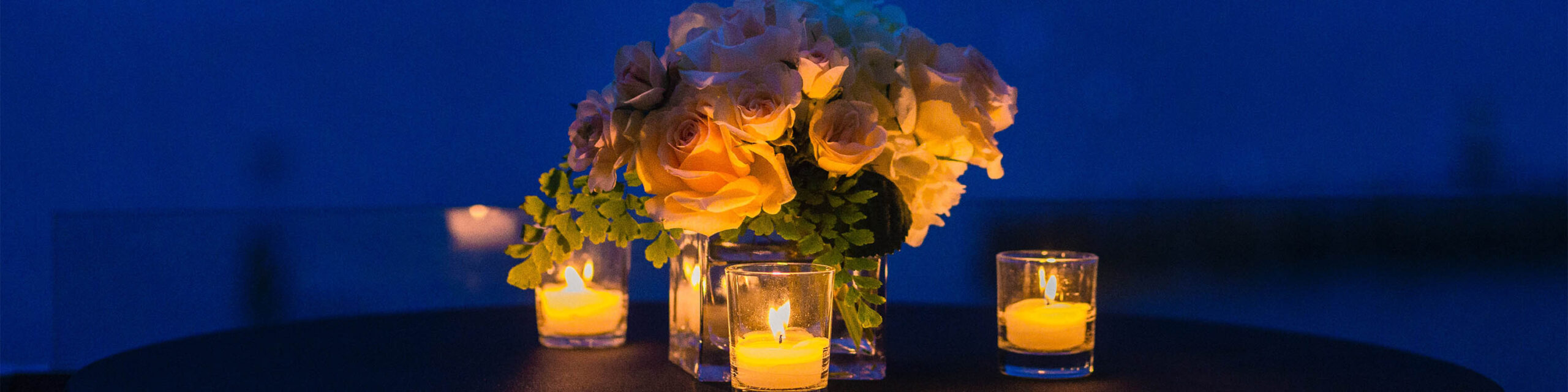 White roses in vase with candles against night backdrop