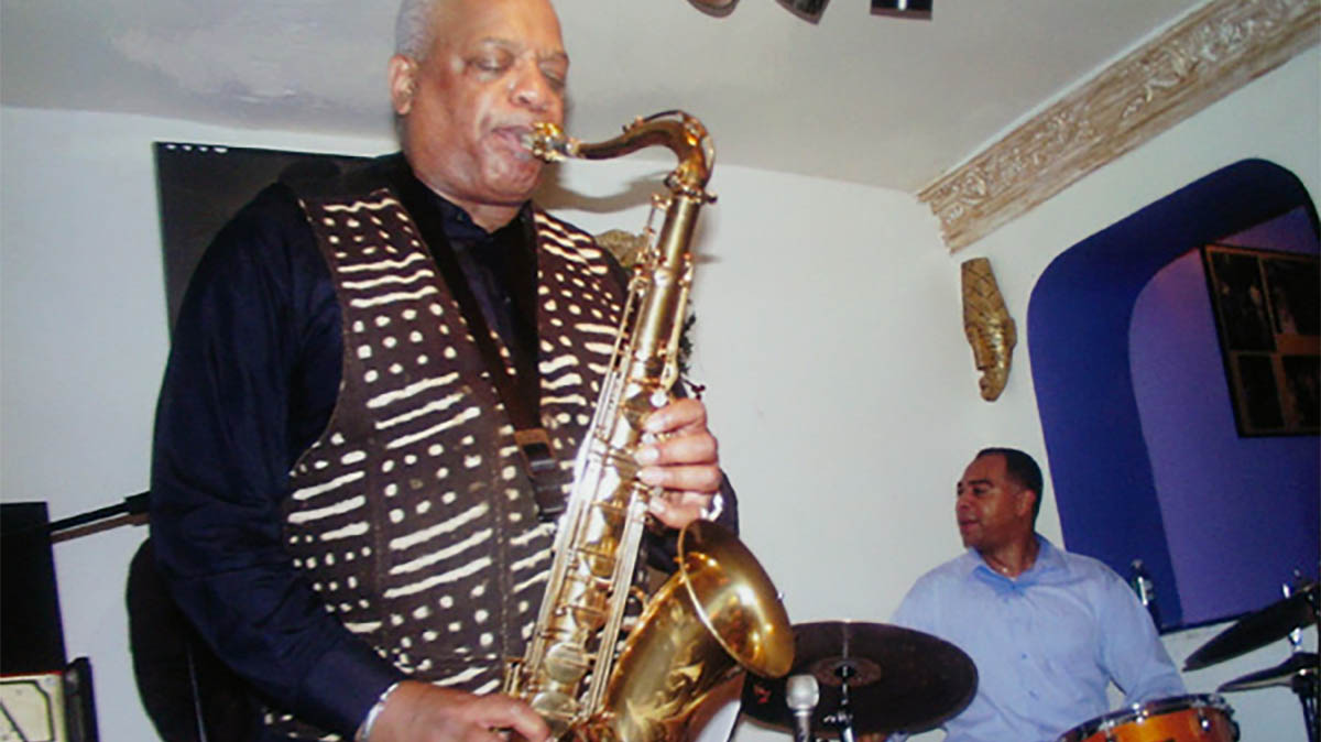Bill Saxton playing saxaphone with background drummer