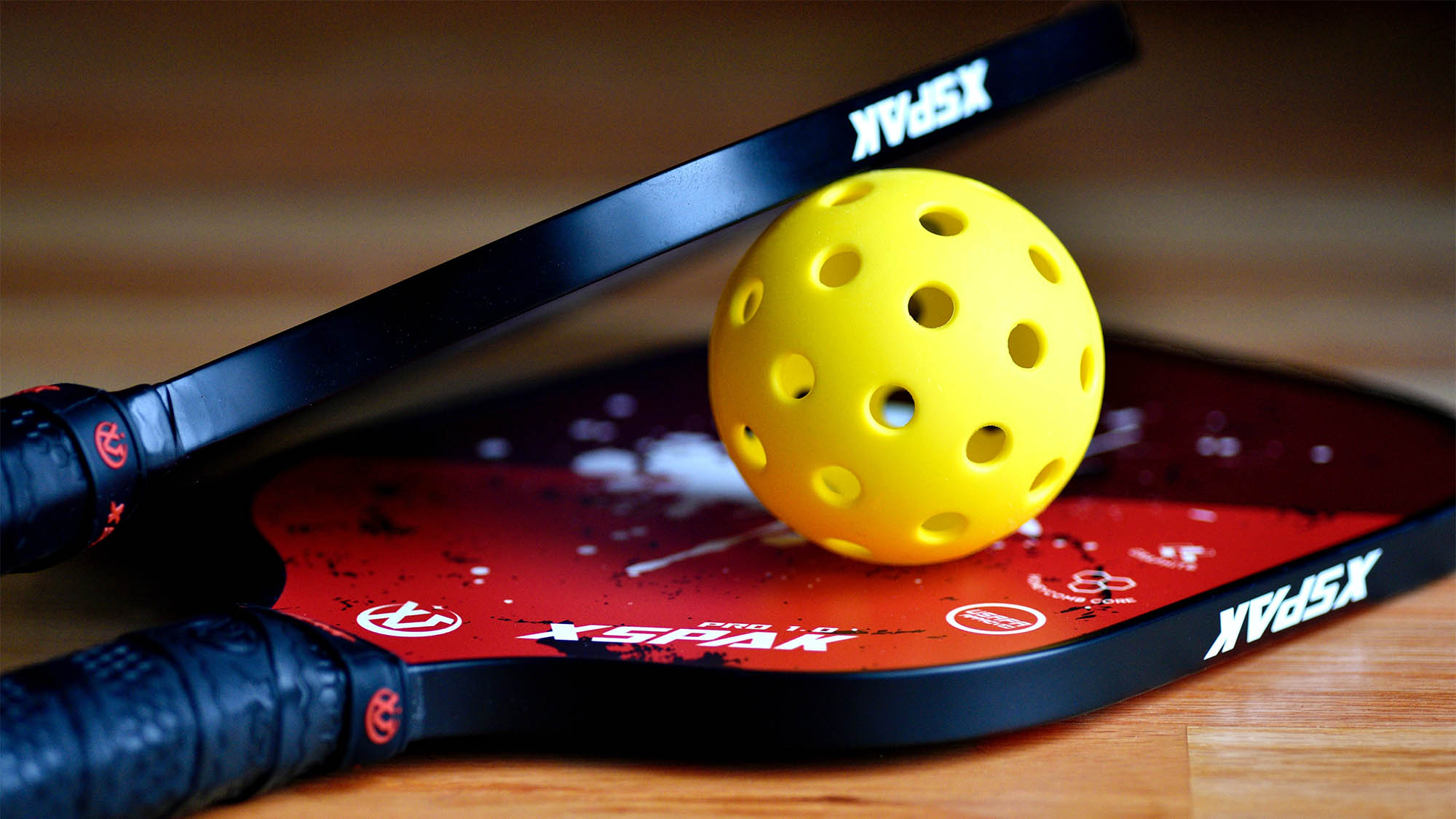 Red and black pickleball rackets with yellow pickleball in between