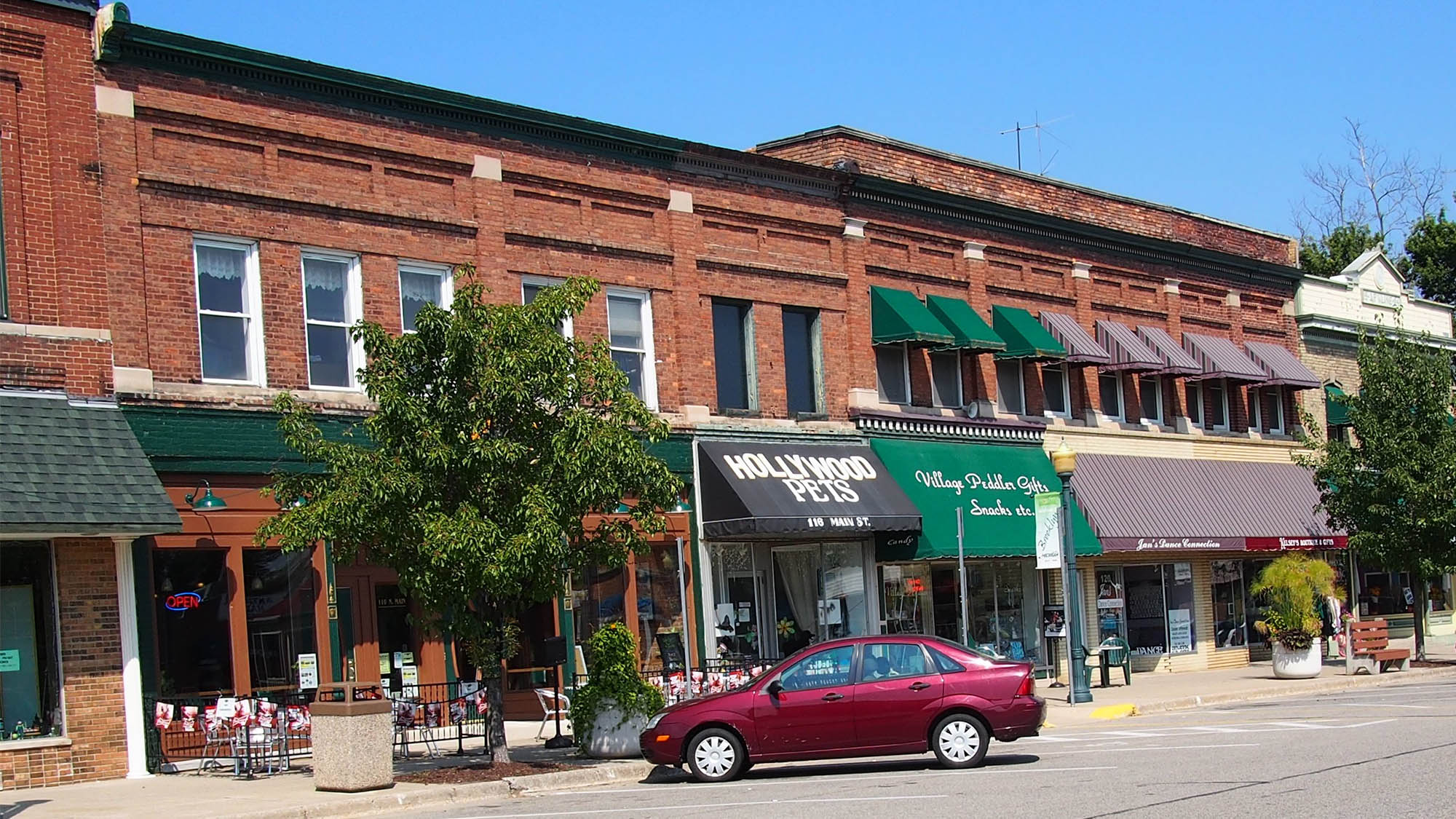 Brick storefronts with old-fashioned awnings and red car parked in front