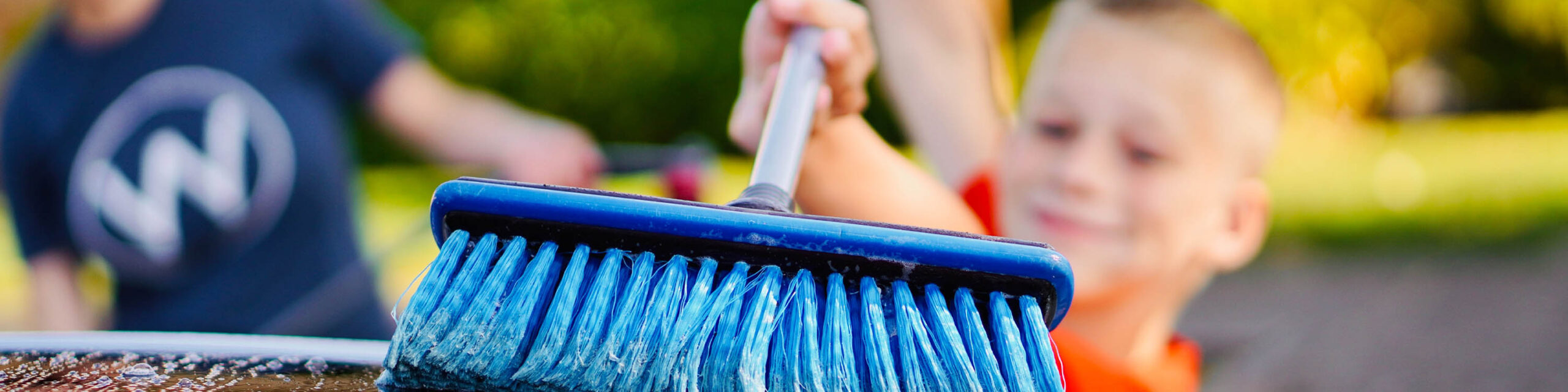 Closeup of blue broom being pushed by blurred out little white boy with blond hair