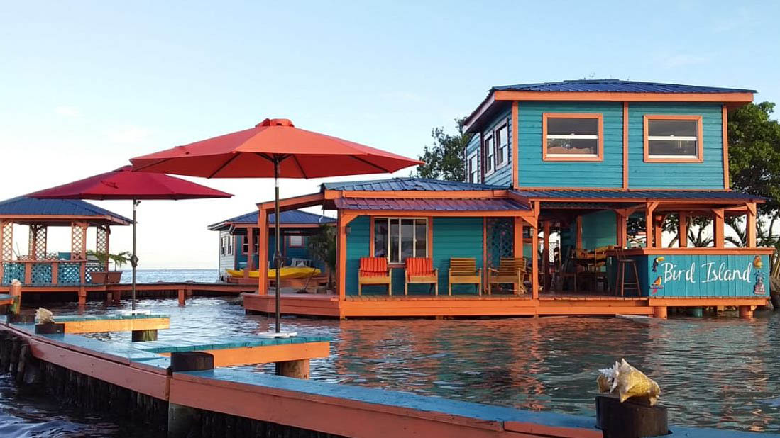 Two story island home rental in water with three umbrellas on left and Big Island mural on right side of building