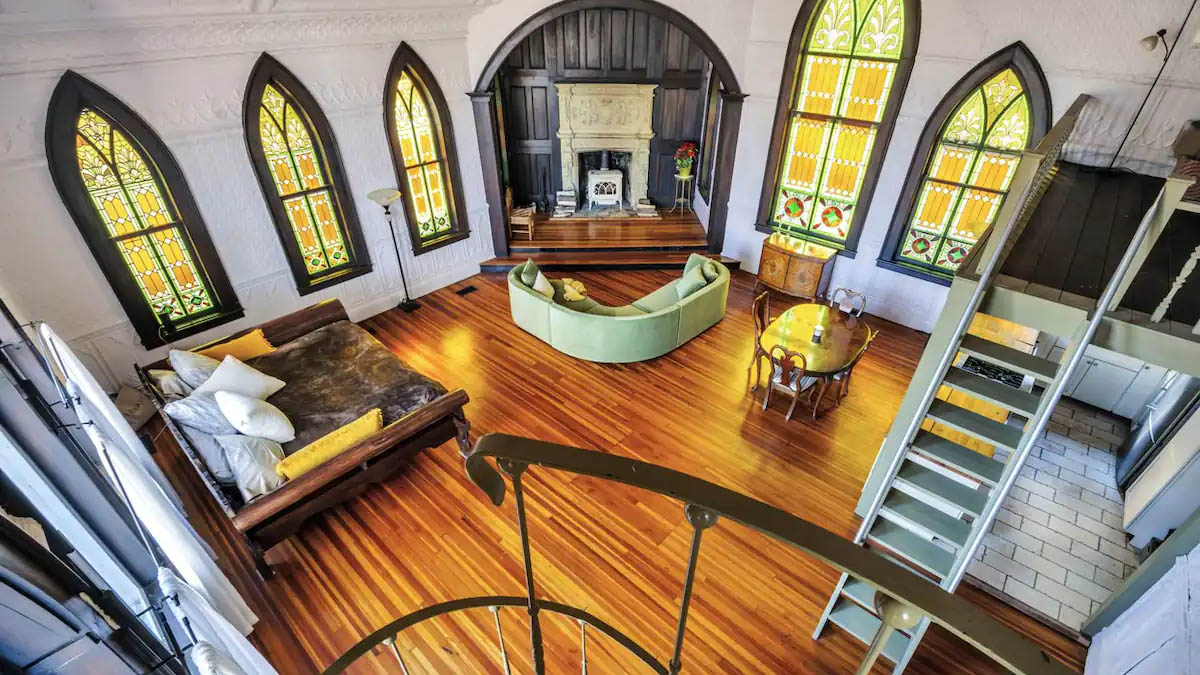 Vacation home interior inside old church with stained-glass windows flanking a fireplace and wood floor