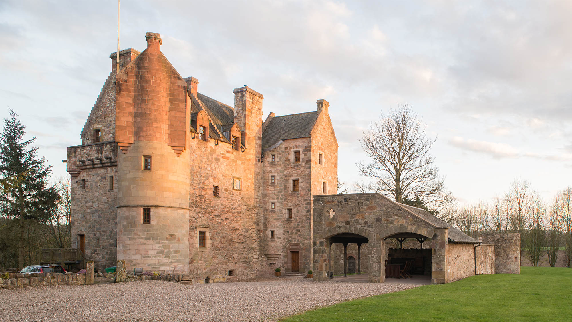 Large restored castle and driveway to the right with trees and lawn in background