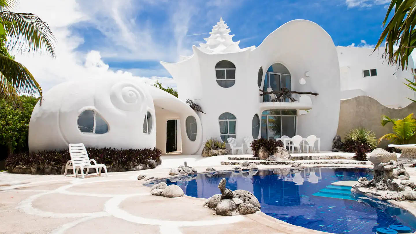 Rear exterior of white shell-shaped mansion with blue pool
