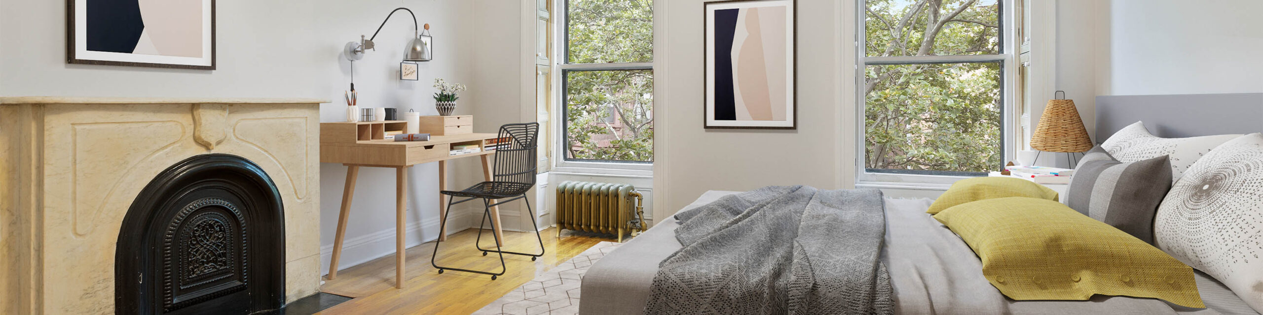 Virtually staged bedroom with fireplace and desk and chair on left and bed on right and two windows and abstract painting on rear wall