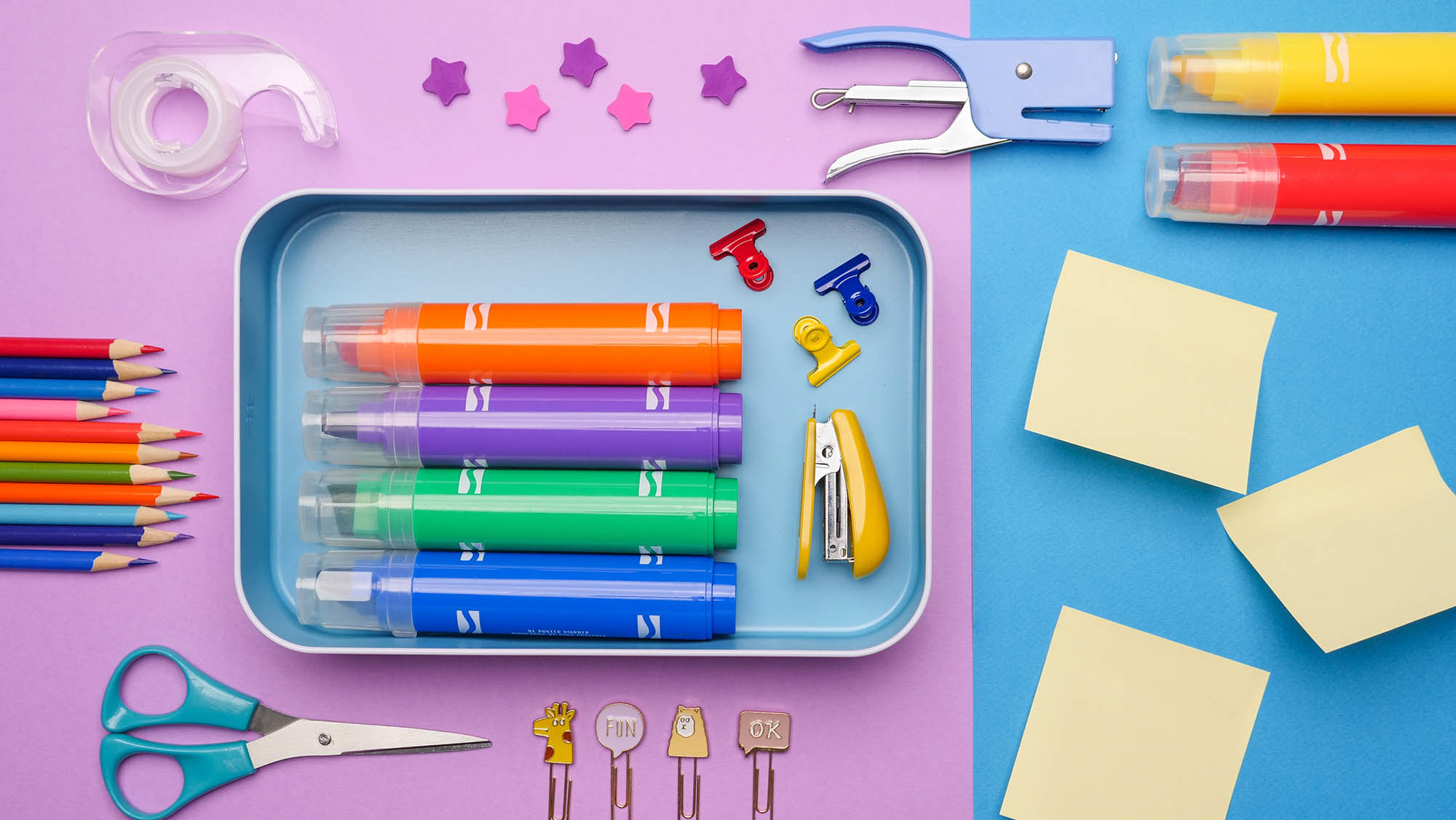 Colorful stationery supplies scattered on purple and blue paper