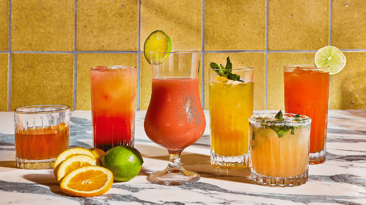 Different cocktails lined up in different glasses with citrus and herb garnishes