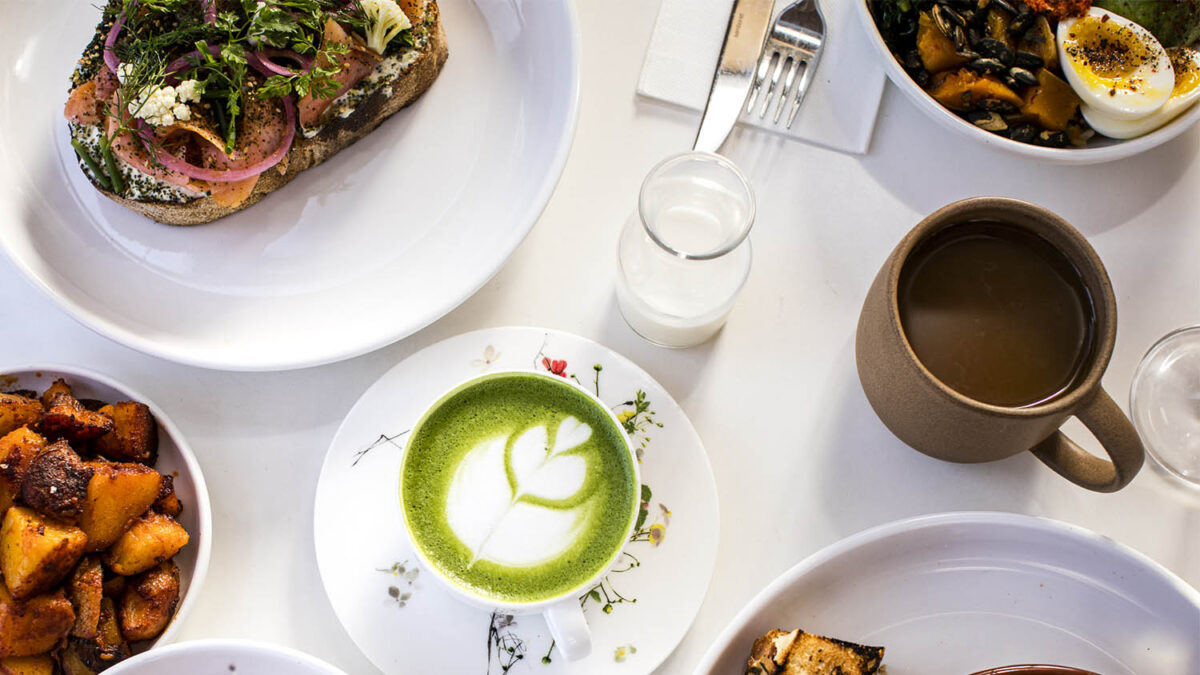 View from above of table with matcha cup, sweet potatoes, vegetable toast, coffee mug and milk on it