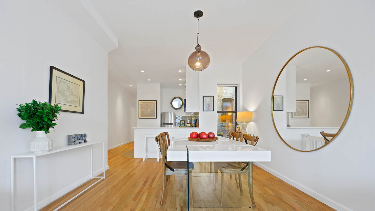 Dining room with pendant light, large round mirror on right wall and framed art on left