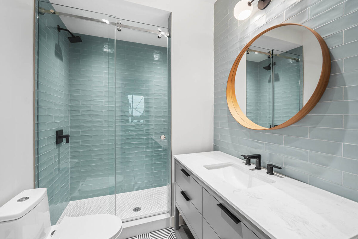 Modern bathroom design with light blue tiled tub and large round statement mirror over sink