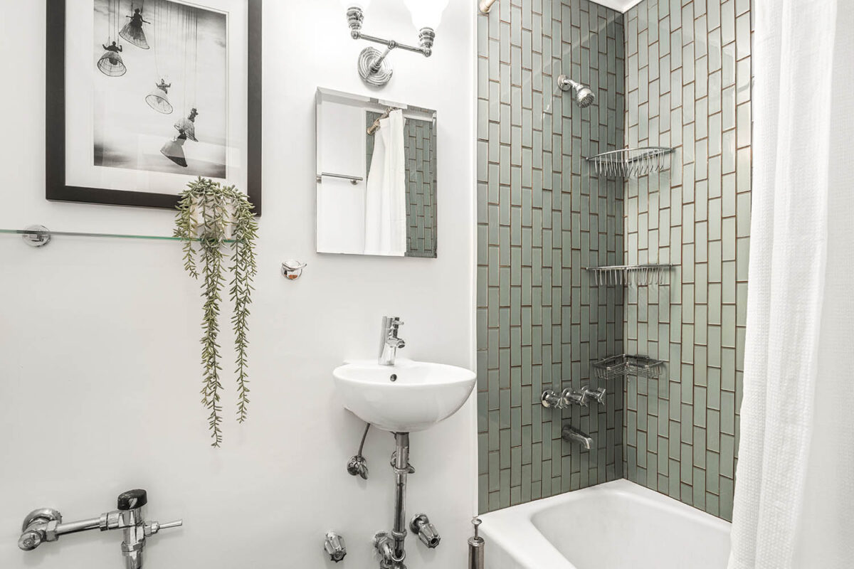 Modern bathroom design with green tiled shower, hanging plant and mirror over vintage sink
