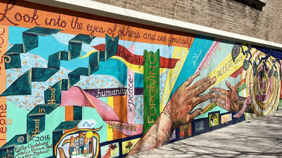 Colorful mural with hands touching that reads: Look Into The Eyes of Others and See Yourself
