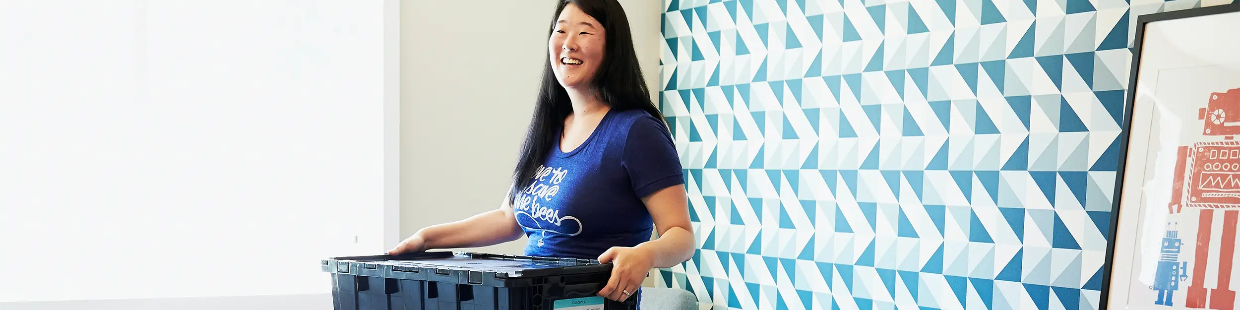 Woman holding moving crate standing in front of geometric wallpaper