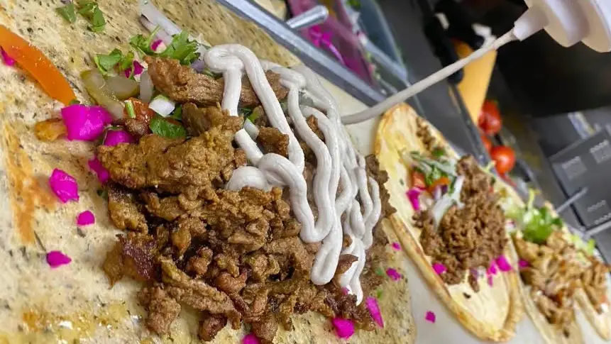 Shawarma sitting atop flatbread while white sauce is being drizzled over it