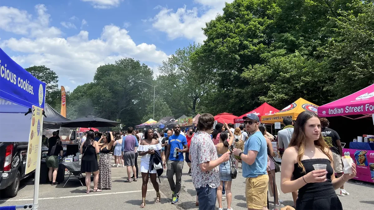 People wandering around a street food market in a park with trees