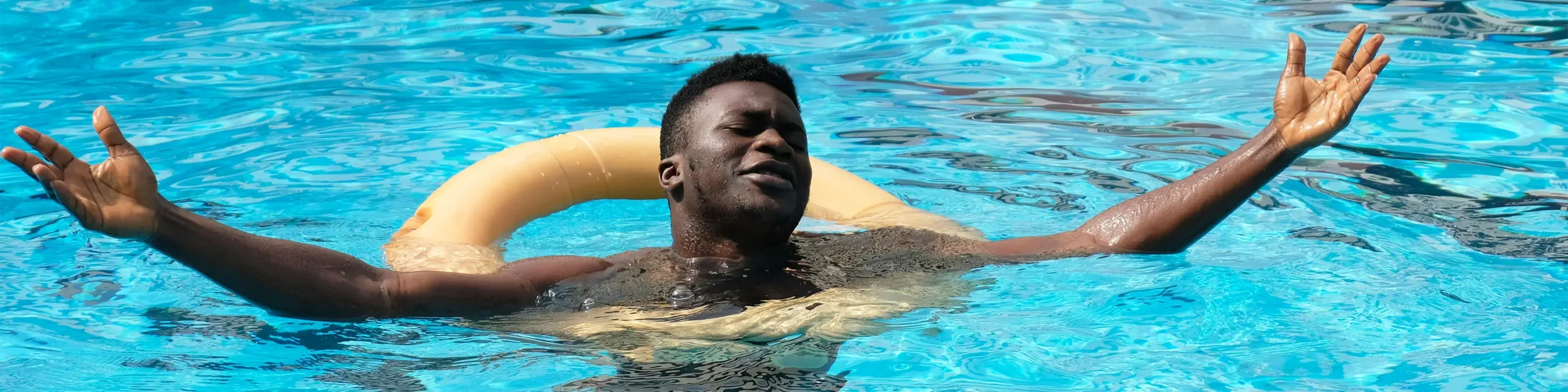 Man in inner tube in pool smiling and holding arms open