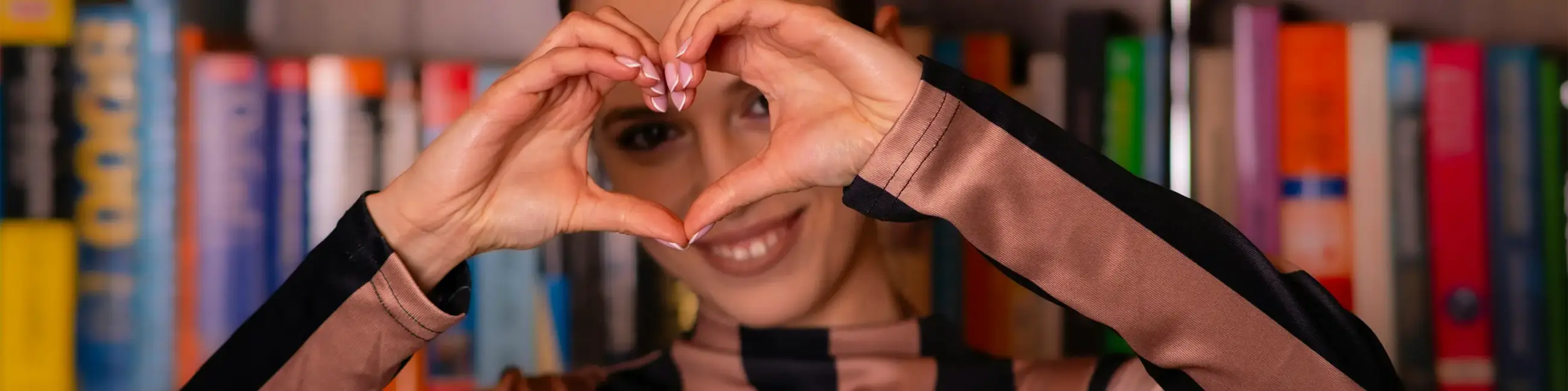 Closeup of woman making heart with hands and library books in background