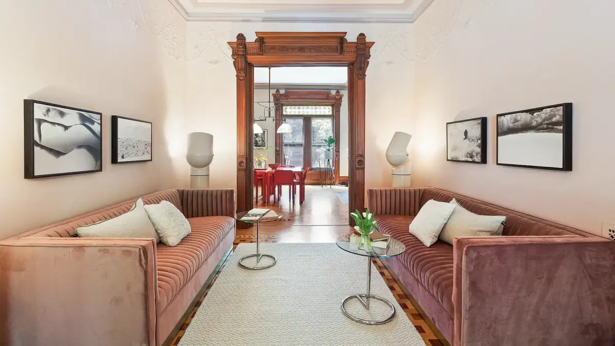 Staged interior with pink couch on either side of narrow room peeking through kitchen in background
